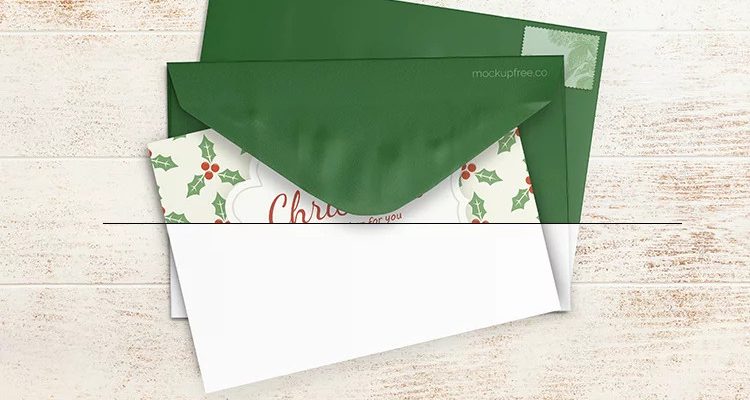 Top-view Christmas card sliding out of a green envelope on a white wooden table