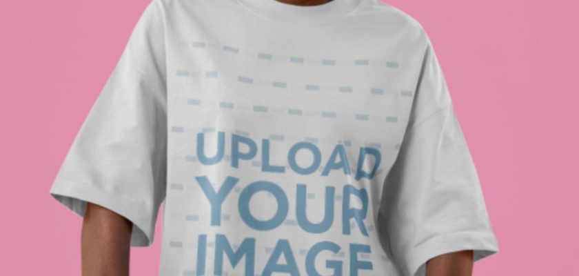Customizable t-shirt mockup of a woman in an oversized white tee and dad hat against a pink studio background