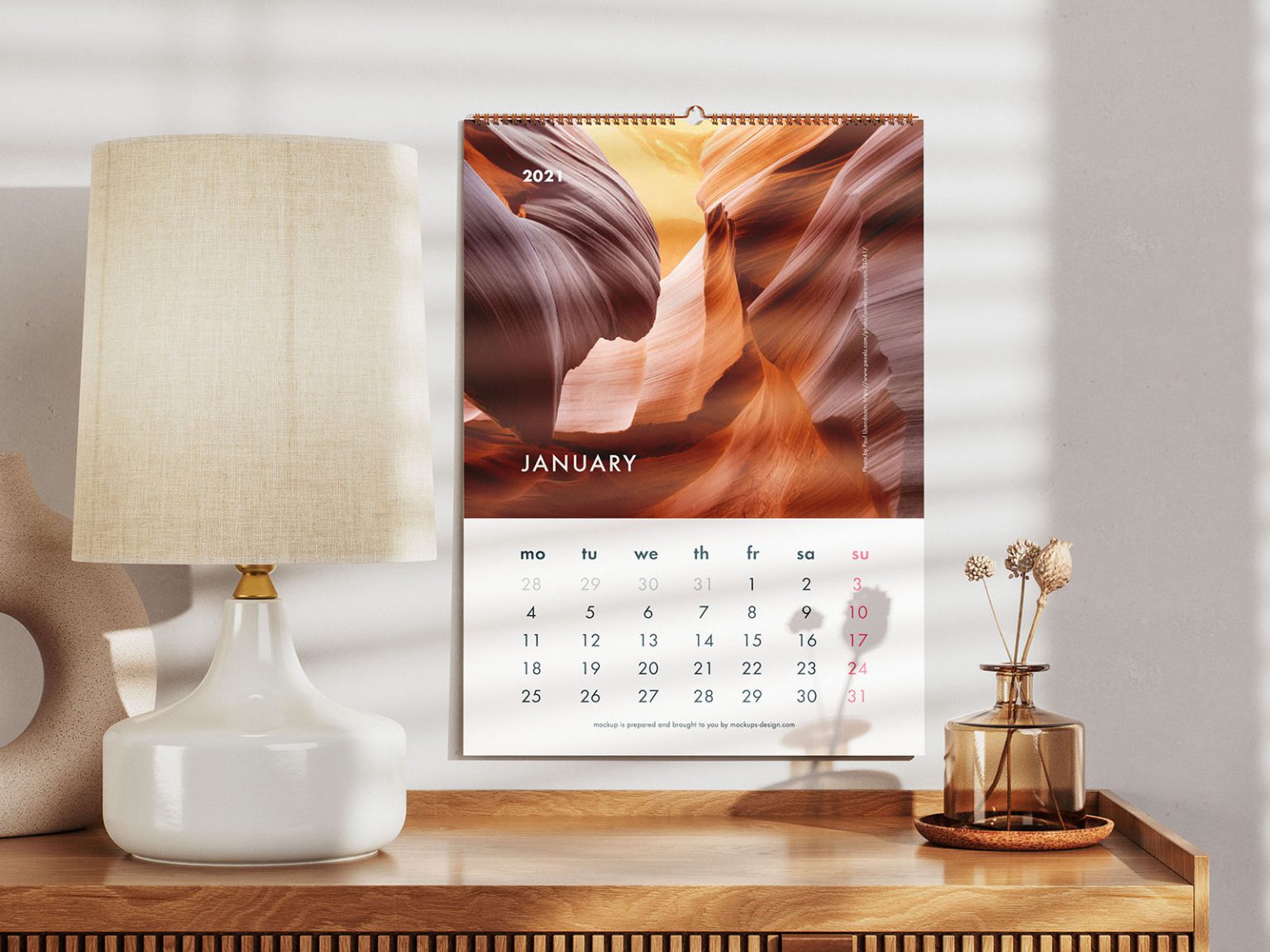 Free calendar mockup PSD — wall calendar above a wooden chest of drawers with a lamp